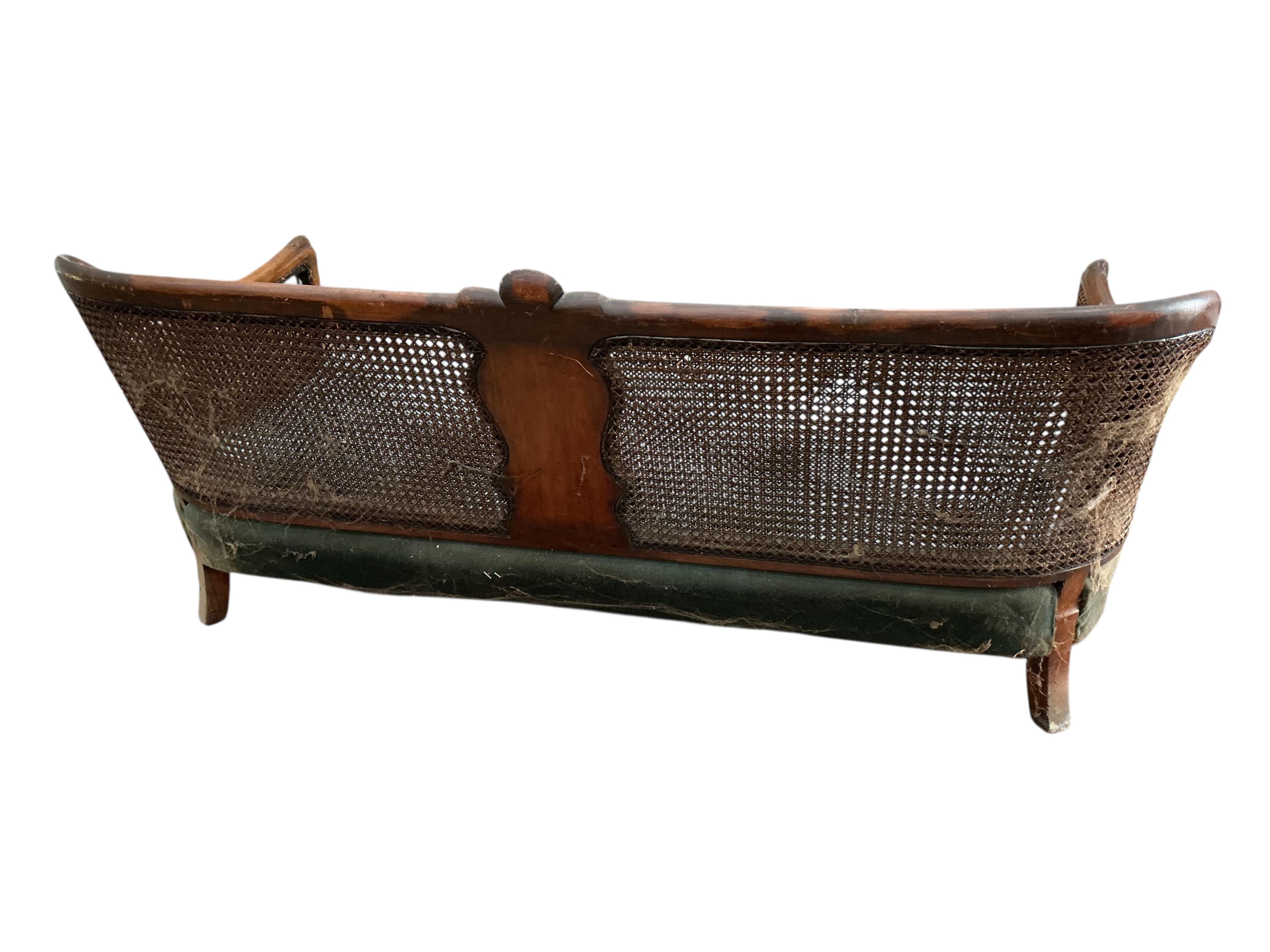 An early 20th century carved walnut and double canework three piece bergère suite, cane in need of repair
